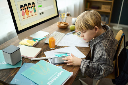 Young boy engaged in studying at desk with various educational tools surrounding him. Computer...