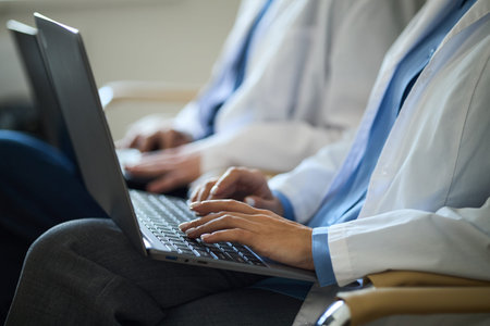 Doctors working on laptops during consultation in hospital setting, wearing white coats and focused...