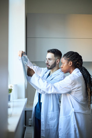 Two medical professionals standing by window, reviewing patient x-rays in clinical setting