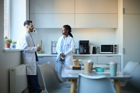 Multiracial healthcare professionals having a discussion in well-lit modern kitchen setting,...