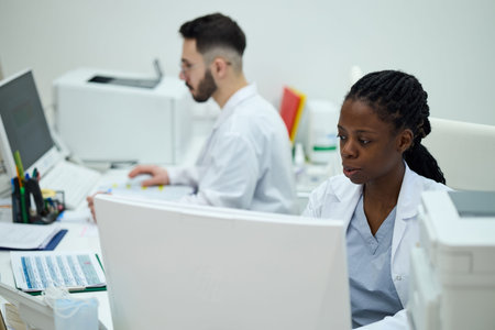 Medical professionals working in a lab environment, analyzing data on computer screens while...