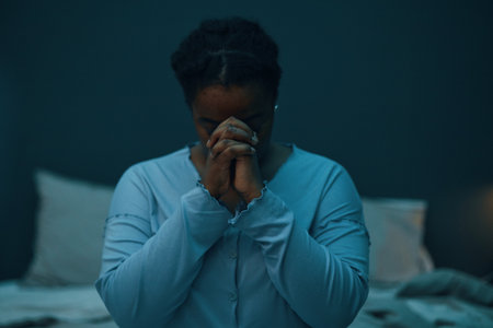Person sitting in dimly lit room with hands clasped together in prayer, conveying calmness and introspection. Dim background enhances tranquil atmosphereの写真素材