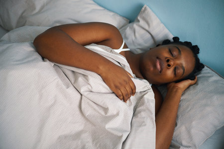 Black woman relaxing peacefully in bed with a gentle expression. Natural lighting illuminating the room, creating a serene and calm atmosphereの写真素材