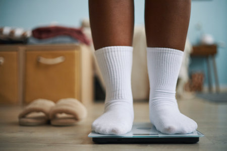 Close-up image showing feet in white socks standing on digital scale in cozy room, focusing on weight measurement and casual home environmentの写真素材
