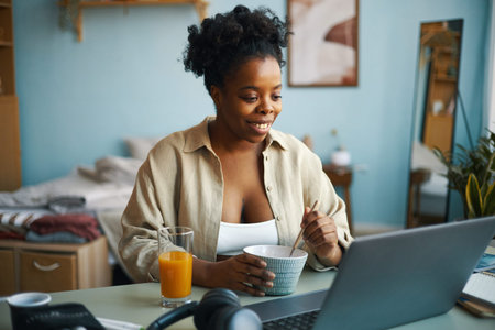 Portrait of African American woman smiling while holding cup and using laptop at home setting