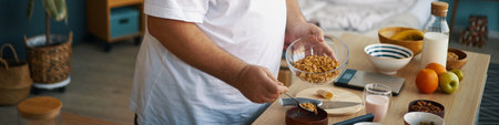 Person is preparing healthy breakfast with fresh ingredients, including granola, fruits, and milk on a kitchen counterの写真素材