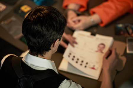 Caucasian young adult woman in uniform holding documents with fingerprints and mugshot, sitting...