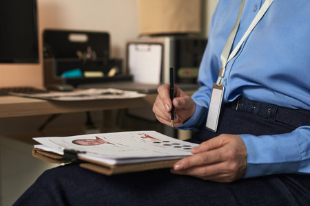 Middle aged Caucasian woman sitting at desk analyzing fingerprint records and mugshot photographs on...