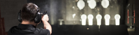 Header of Caucasian middle aged man wearing protective earmuffs practicing shooting with handgun at...