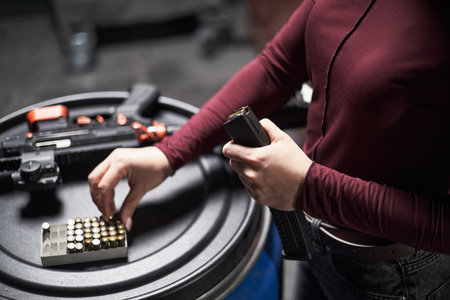 Anonymous woman loading magazine with ammunition standing next to rifle on round table in shooting club preparing for target practice sessionの写真素材