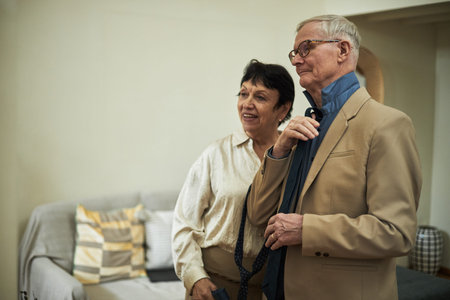 Elderly couple standing in a cozy living room, looking content and comfortable. Both are wearing...