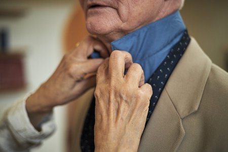 Close-up of female hands adjusting blue shirt collar for elderly gentleman wearing suit coat and...