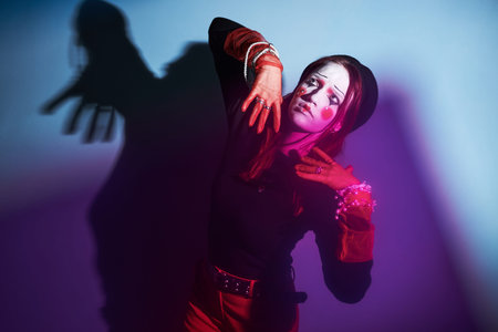 Caucasian teenage girl wearing creative makeup posing dramatically with hands raised near face, performing expressive gesture in colorful lighting at home, embodying Gen Z creativityの写真素材