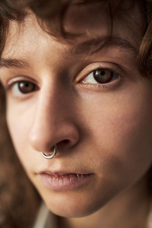 Portrait of Caucasian teenager girl with nose ring looking into camera, close up of face showing...