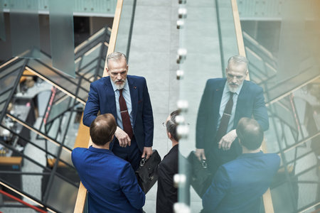 Group of businessmen in heated discussion, standing in modern office with glass staircase. Office...