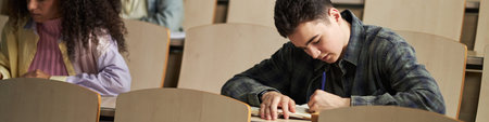 Header of Caucasian teenage boy sitting in lecture hall writing in notebook, multiethnic girl...