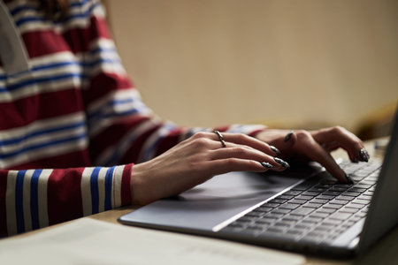 Hands of young woman typing on laptop keyboard, with manicured nails and ring, studying or working...