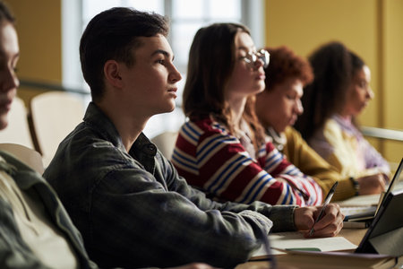 Group of multiethnic university students sitting in classroom listening attentively, young adult and teenager men and women taking notes and using laptops during lectureの写真素材