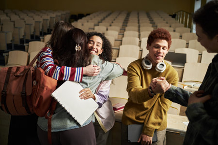 Group of multiethnic university students greeting each other in lecture hall, young women hugging...