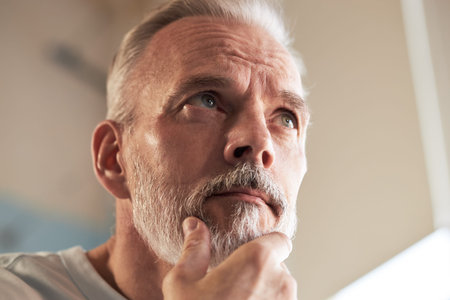 Portrait of middle aged Caucasian man touching beard and looking thoughtfully upward, showing skincare routine concept with closeup focus on facial features and groomingの写真素材