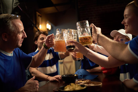 Group of happy young Caucasian and Black male and female fans celebrating with beer mugs in sports...