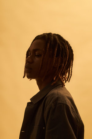 Black teenager boy standing in profile with serious expression, looking away from camera against...