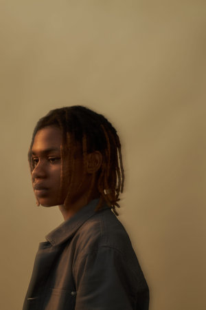 Black teenager boy standing in profile with serious expression, looking away from camera against...