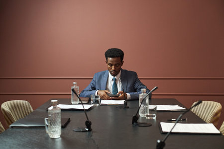 Young adult Black man sitting at conference table preparing for political meeting, checking...