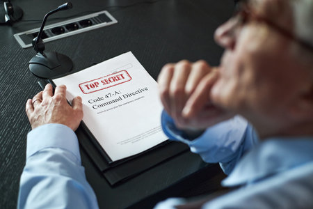 Senior Caucasian man sitting at conference table holding classified document labeled top secret, resting hand on folder, appearing thoughtful, microphone visible nearbyの写真素材