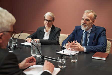 Middle aged Caucasian man and middle aged Caucasian woman sitting at conference table discussing...