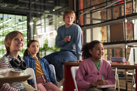 Group of diverse children and teenagers sitting together in modern classroom, Caucasian boy holding...