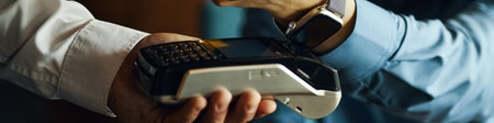 Caucasian man holding payment terminal while young adult Caucasian man wearing smartwatch making...