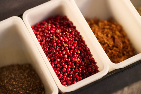 Closeup showing containers filled with red peppercorns, dried herbs, and spices arranged in row, emphasizing variety of culinary ingredients used for cooking and seasoning foodの写真素材