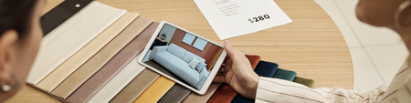 Two young adult Caucasian women sitting at round table reviewing sofa options on digital tablet,...