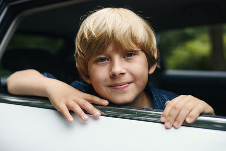 Portrait of Caucasian boy child smiling and leaning out car window during family road trip, hands...