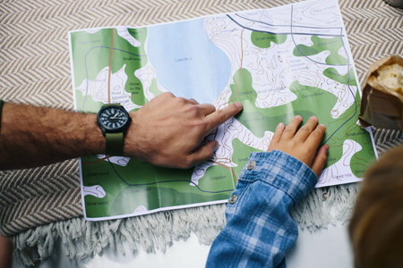 Caucasian middle aged man and Caucasian child studying map together during family road trip, adult...