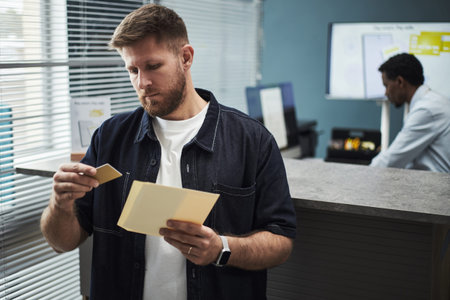 Caucasian young man holding credit card and reading document near counter in bank office, Black...