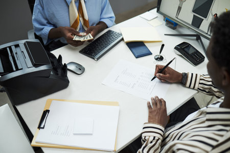 Black male customer signing financial documents while female clerk is counting cash at desk in bank...