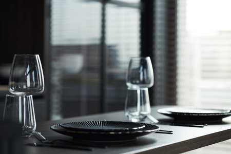 Empty dining table set with two black plates, two wine glasses, two water glasses and cutlery...
