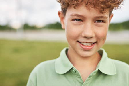 Portrait of Caucasian boy smiling outdoors, looking into camera, standing in park or open field, curly hair visible, casual expression, natural backgroundの写真素材
