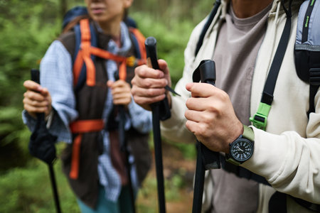 Young adult Caucasian man and young adult woman hiking in forest holding trekking poles, wearing backpacks, focusing on hands and upper bodies, exploring nature togetherの写真素材
