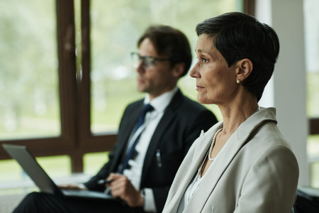 Middle aged Caucasian woman sitting in profile with short hair, wearing business attire, listening...