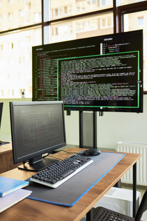 Modern workspace featuring desktop computer and large monitor displaying programming code,...