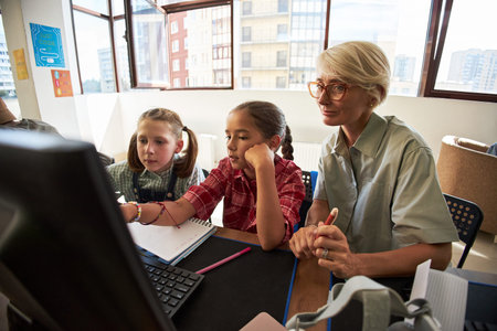 Caucasian middle aged woman assisting two girls, one Caucasian and one possibly Hispanic, working...
