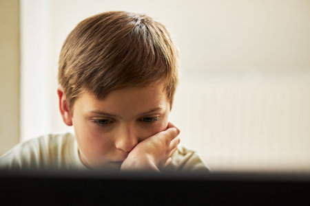 Portrait of Caucasian boy child resting chin on hand while looking at computer screen, concentrating...