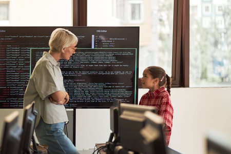 Middle aged Caucasian woman standing and talking with preteen girl in computer classroom, large...