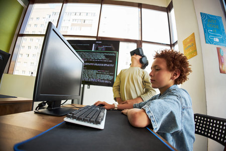 Two boys in classroom using technology, Caucasian child sitting at desk typing on computer keyboard...