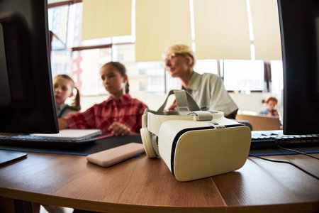 Caucasian senior woman teaching two Caucasian children using desktop computers in classroom, virtual...