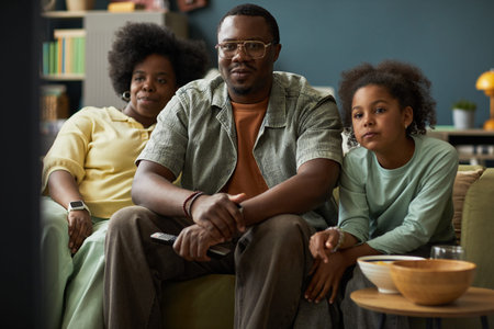 Portrait of man sitting on sofa with woman and child girl watching television together in living...