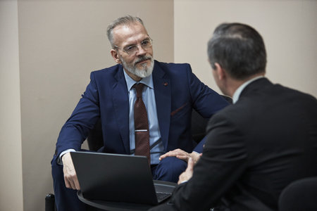 Middle aged Caucasian man with gray beard sitting in business meeting with male partner, discussing...